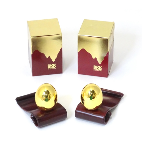 257 - Two Risis models of eggs covered in 999 gold with wooden stands and boxed. (2)