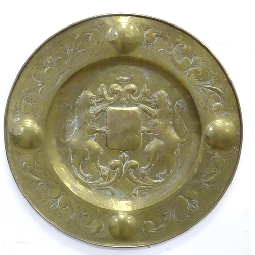 888 - A large brass charger with embossed heraldic crest decoration with lions and shield to centre. Appro... 