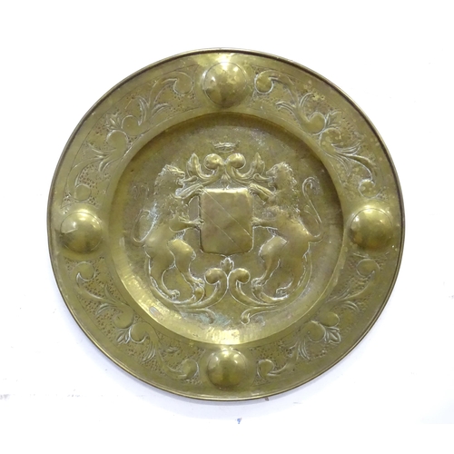 888 - A large brass charger with embossed heraldic crest decoration with lions and shield to centre. Appro... 