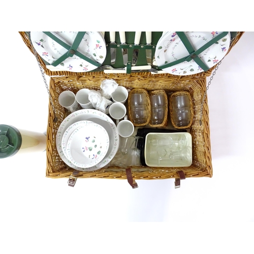 630 - A wicker picnic basket containing plastic plates, bowls, mugs, etc. with floral decoration, cutlery,... 