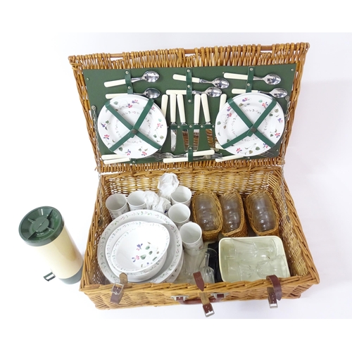 630 - A wicker picnic basket containing plastic plates, bowls, mugs, etc. with floral decoration, cutlery,... 