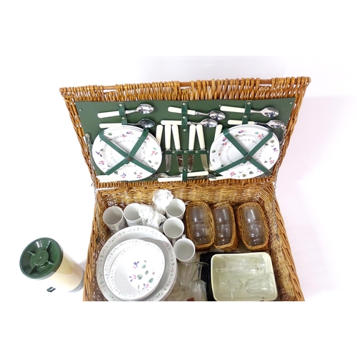 630 - A wicker picnic basket containing plastic plates, bowls, mugs, etc. with floral decoration, cutlery,... 