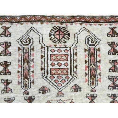 1380 - Carpet / Rug: A beige ground rug with repeated motifs worked in salmon pink, brown and beige, with b... 