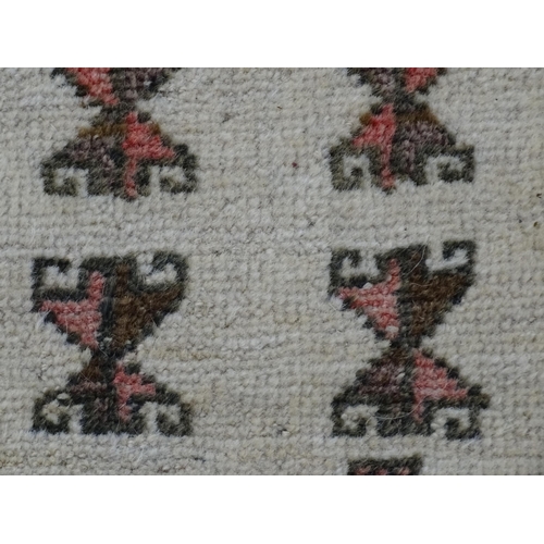 1380 - Carpet / Rug: A beige ground rug with repeated motifs worked in salmon pink, brown and beige, with b... 