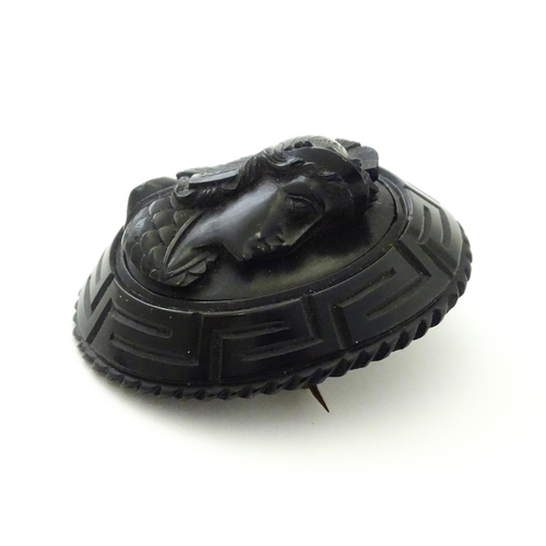 761 - A Victorian Whitby jet cameo brooch depicting the head of a Roman solider, within a Greek key mount.... 