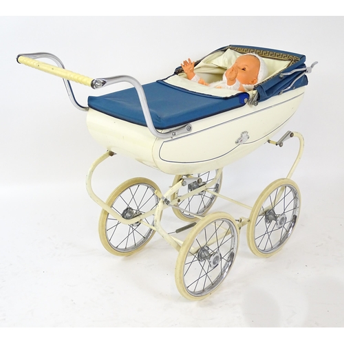 956A - Toys: A 20thC Pedigree dolls pram with cream exterior and blue hood. Together with a plastic doll wi... 