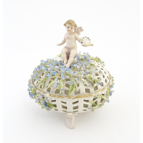 104 - A Continental basket and cover with pierced detail and encrusted flowers surmounted by a putto / che... 