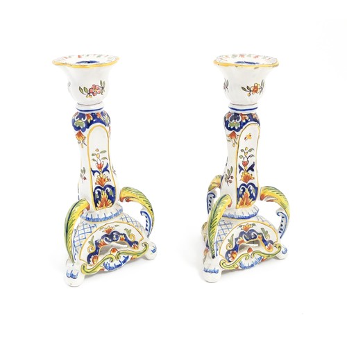 106 - A pair of French faience candlesticks with shaped bases, decorated with flowers and foliage. Marked ... 