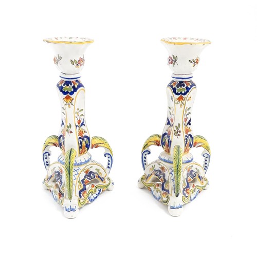 106 - A pair of French faience candlesticks with shaped bases, decorated with flowers and foliage. Marked ... 