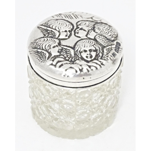 290 - A cut glass dressing table / toilet jar with embossed silver top decorated with cherubs, hallmarked ... 