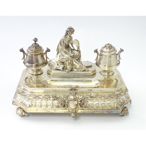 454 - A silver desk standish with Classical muse flanked by two urn formed inkwells and recessed pen well,... 