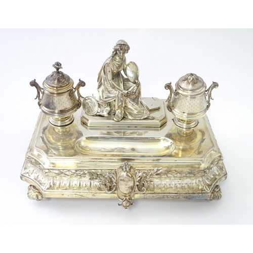 454 - A silver desk standish with Classical muse flanked by two urn formed inkwells and recessed pen well,... 