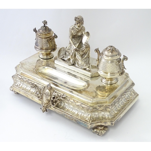 454 - A silver desk standish with Classical muse flanked by two urn formed inkwells and recessed pen well,... 