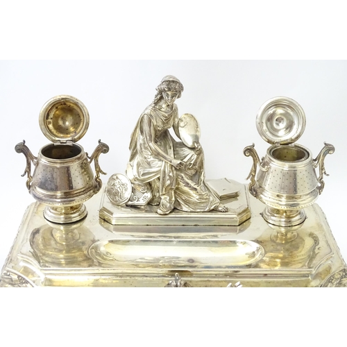 454 - A silver desk standish with Classical muse flanked by two urn formed inkwells and recessed pen well,... 