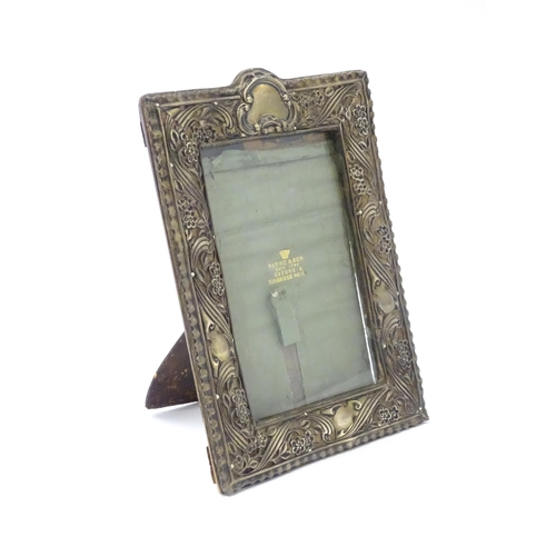 484 - An Art Nouveau easel back photograph frame with a silver surround with embossed floral decoration, h... 