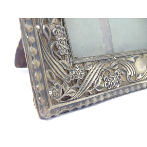 484 - An Art Nouveau easel back photograph frame with a silver surround with embossed floral decoration, h... 