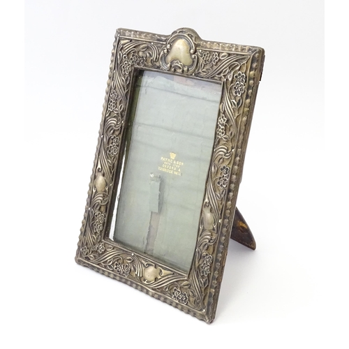 484 - An Art Nouveau easel back photograph frame with a silver surround with embossed floral decoration, h... 