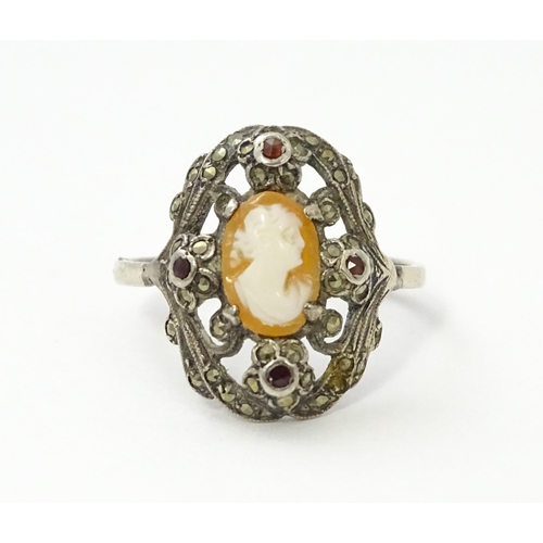 555 - A white metal ring set with central shell carved cameo detail bordered by garnet and marcasite detai... 