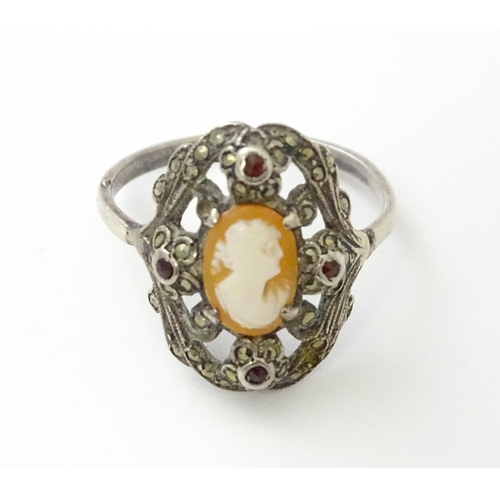 555 - A white metal ring set with central shell carved cameo detail bordered by garnet and marcasite detai... 