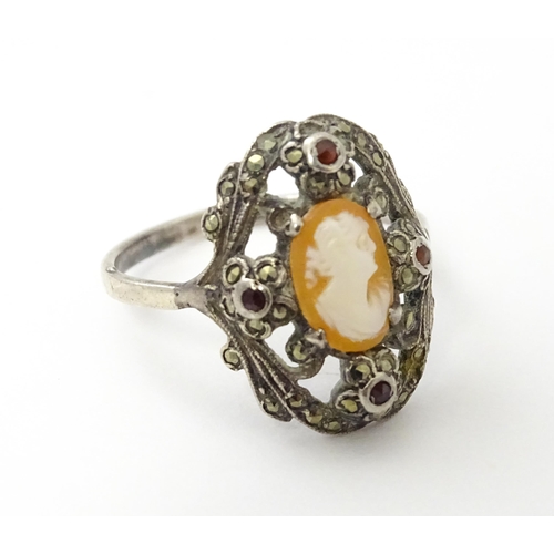 555 - A white metal ring set with central shell carved cameo detail bordered by garnet and marcasite detai... 