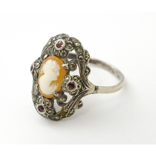 555 - A white metal ring set with central shell carved cameo detail bordered by garnet and marcasite detai... 