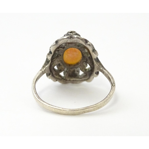 555 - A white metal ring set with central shell carved cameo detail bordered by garnet and marcasite detai... 