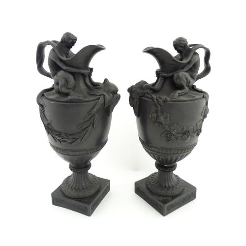 A pair of Wedgwood black basalt wine and water ewers, the wine ewer Sacred to Bacchus, with seated Bacchus holding the spout, and applied goat head and fruiting vine wreath detail, the water ewer Sacred to Neptune with seated Neptune holding the spout, and applied dolphin mask and seaweed wreath detail. Impressed marks under. Approx. 15 1/2" high (2)