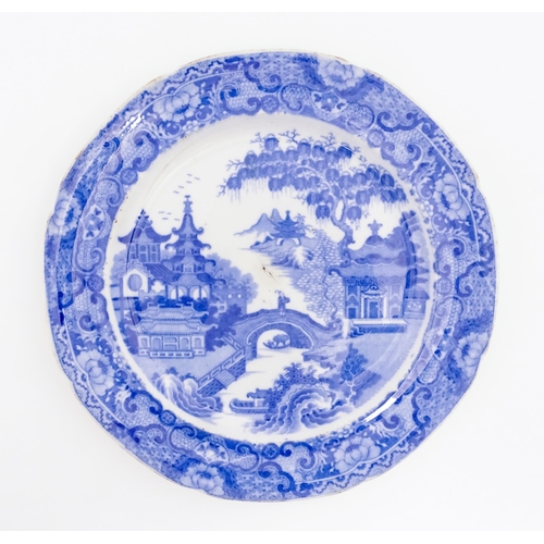 65 - A 19thC blue and white plate decorated with a river landscape with ornate pagodas and a figure on a ... 