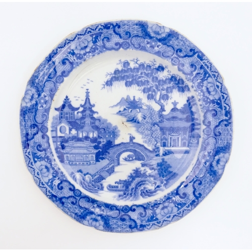 65 - A 19thC blue and white plate decorated with a river landscape with ornate pagodas and a figure on a ... 