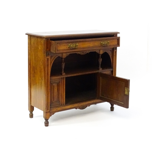 1629 - An Aesthetic movement walnut side cabinet with a chamfered frame and carved floral decoration, the c... 