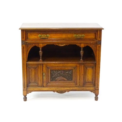 1629 - An Aesthetic movement walnut side cabinet with a chamfered frame and carved floral decoration, the c... 