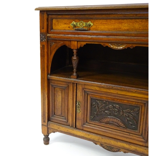 1629 - An Aesthetic movement walnut side cabinet with a chamfered frame and carved floral decoration, the c... 