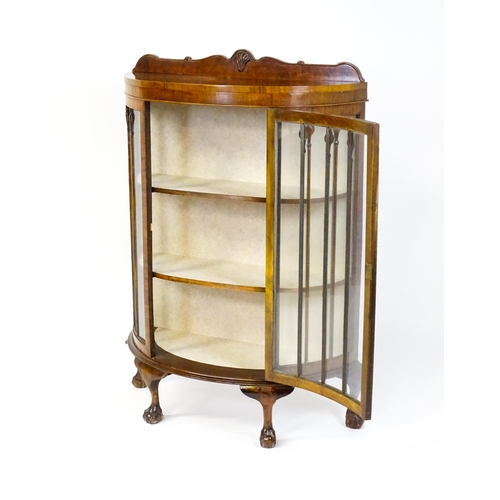 1669 - An early / mid 20thC walnut demi lune display cabinet with a shaped and carved upstand above a singl... 