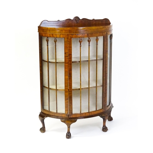 1669 - An early / mid 20thC walnut demi lune display cabinet with a shaped and carved upstand above a singl... 