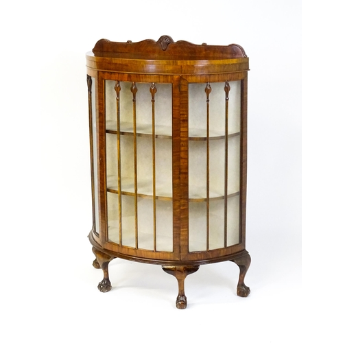 1669 - An early / mid 20thC walnut demi lune display cabinet with a shaped and carved upstand above a singl... 