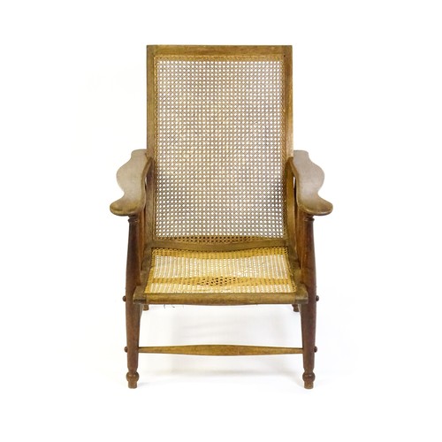 1693 - An Arts & Crafts bergere chair with a caned backrest and seat, the shaped arms supported by turned t... 