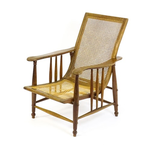 1693 - An Arts & Crafts bergere chair with a caned backrest and seat, the shaped arms supported by turned t... 