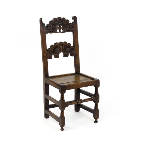 1720 - A 17thC oak peg jointed hall chair / back stool with a carved and scrolled top and mid rail raised o... 