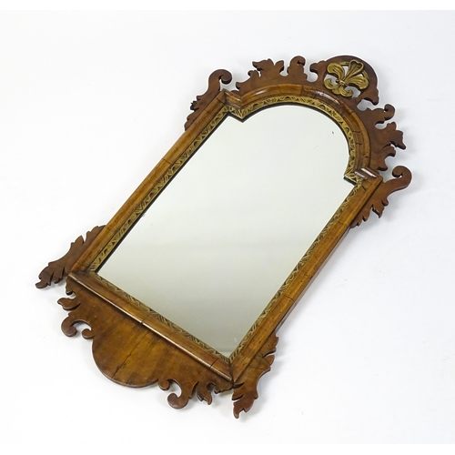 1610 - An early 20thC walnut wall mirror surmounted by a gilt Fleur de Lys, carved scrolled decoration and ... 