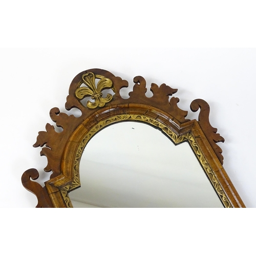 1610 - An early 20thC walnut wall mirror surmounted by a gilt Fleur de Lys, carved scrolled decoration and ... 