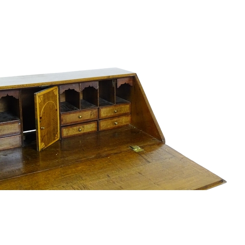 1662 - A Georgian oak bureau with a fall front opening to show crossbanded drawers, a marquetry inlaid door... 