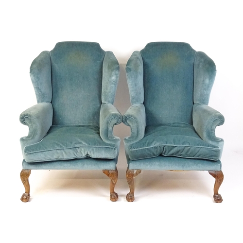 1691 - A pair of early 20thC wingback armchairs with scrolled arms and raised on acanthus carved cabriole f... 