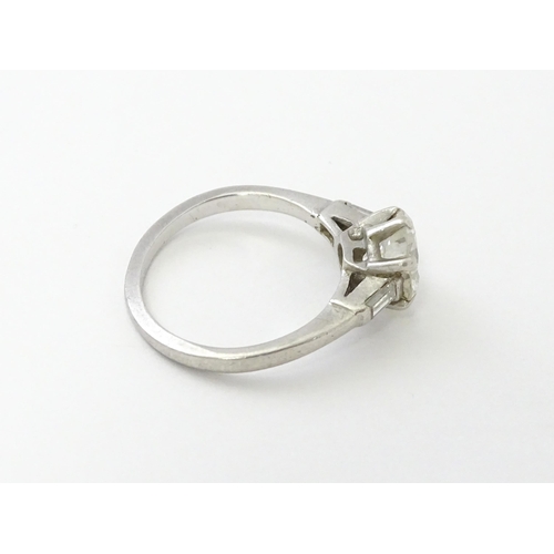 567 - A platinum set brilliant diamond solitaire ring flanked by two baguette cut diamonds to shoulders. C... 