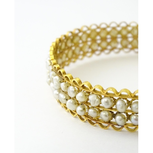 594 - A gold (tested) bracelet of bangle form set with two rows of banded pearls in a rope twist setting. ... 