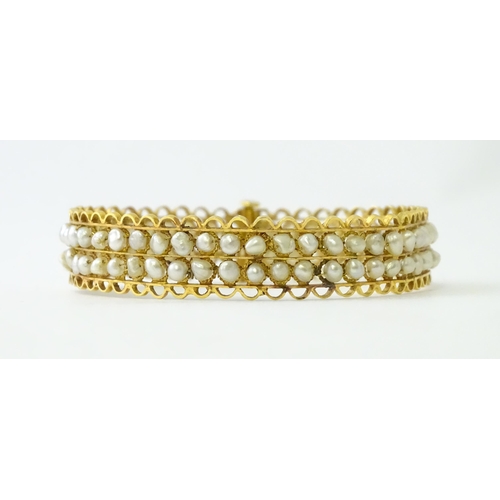 594 - A gold (tested) bracelet of bangle form set with two rows of banded pearls in a rope twist setting. ... 