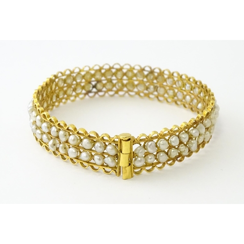 594 - A gold (tested) bracelet of bangle form set with two rows of banded pearls in a rope twist setting. ... 