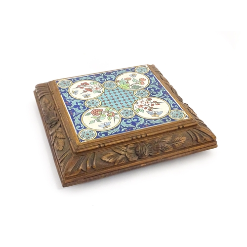 1287 - A 20thC carved wooden teapot stand set with Longwy tile to top having floral and foliate decoration,... 