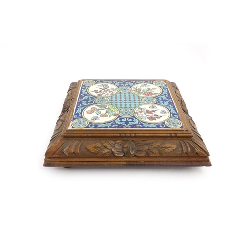 1287 - A 20thC carved wooden teapot stand set with Longwy tile to top having floral and foliate decoration,... 