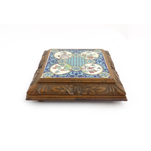 1287 - A 20thC carved wooden teapot stand set with Longwy tile to top having floral and foliate decoration,... 