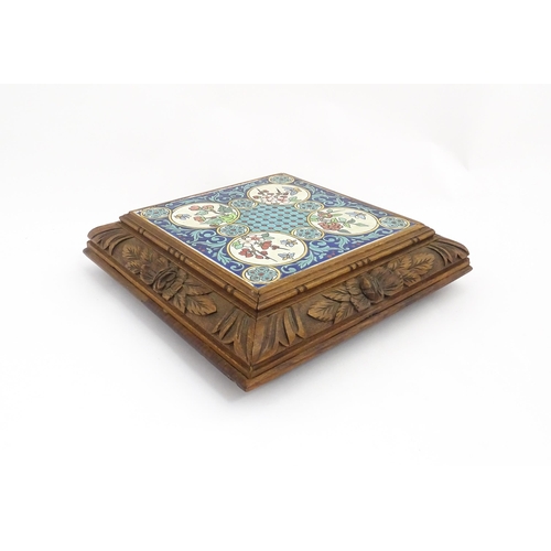 1287 - A 20thC carved wooden teapot stand set with Longwy tile to top having floral and foliate decoration,... 